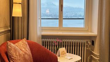 A room with a large window, a red armchair, a small table with a book and a vase of flowers, and a radiator.