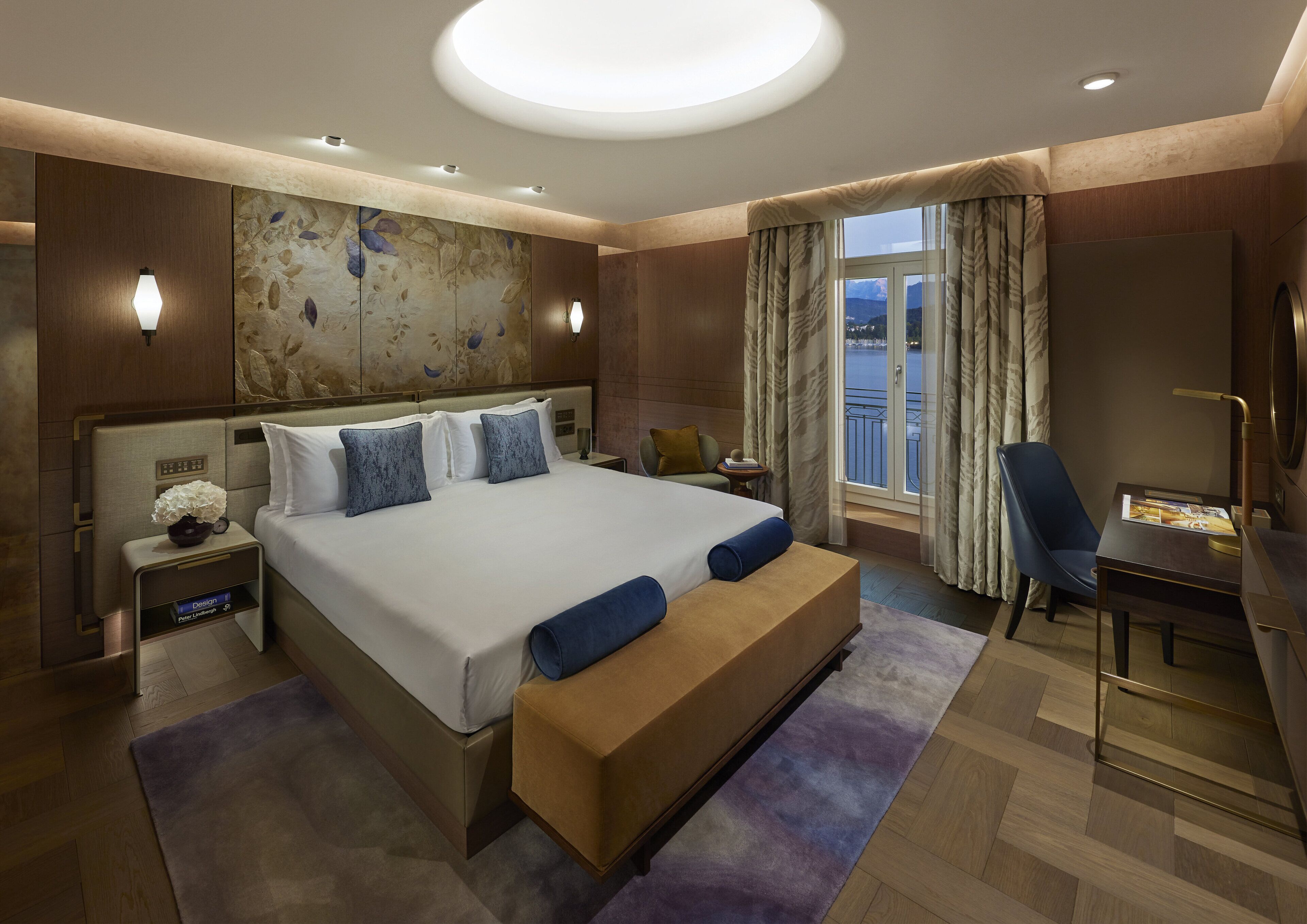 A modern hotel room with a large bed, a desk, and a view of the outdoors.