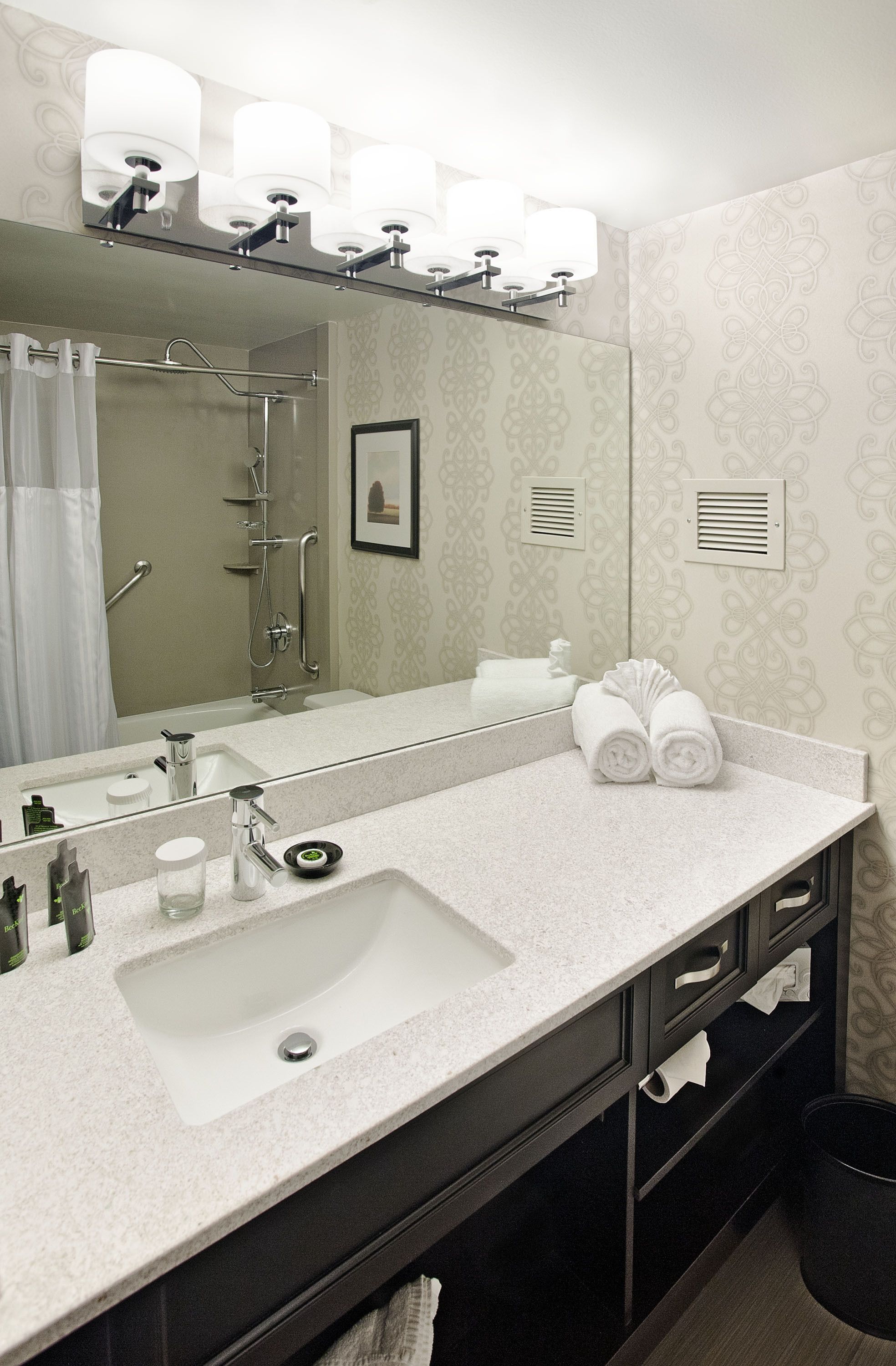Un baño moderno con un espejo grande, un lavabo, una ducha y un perchero para toallas.