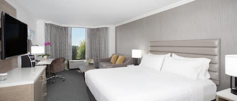 Habitación de hotel con una cama grande, un escritorio con computadora, televisión y ventana con cortinas.