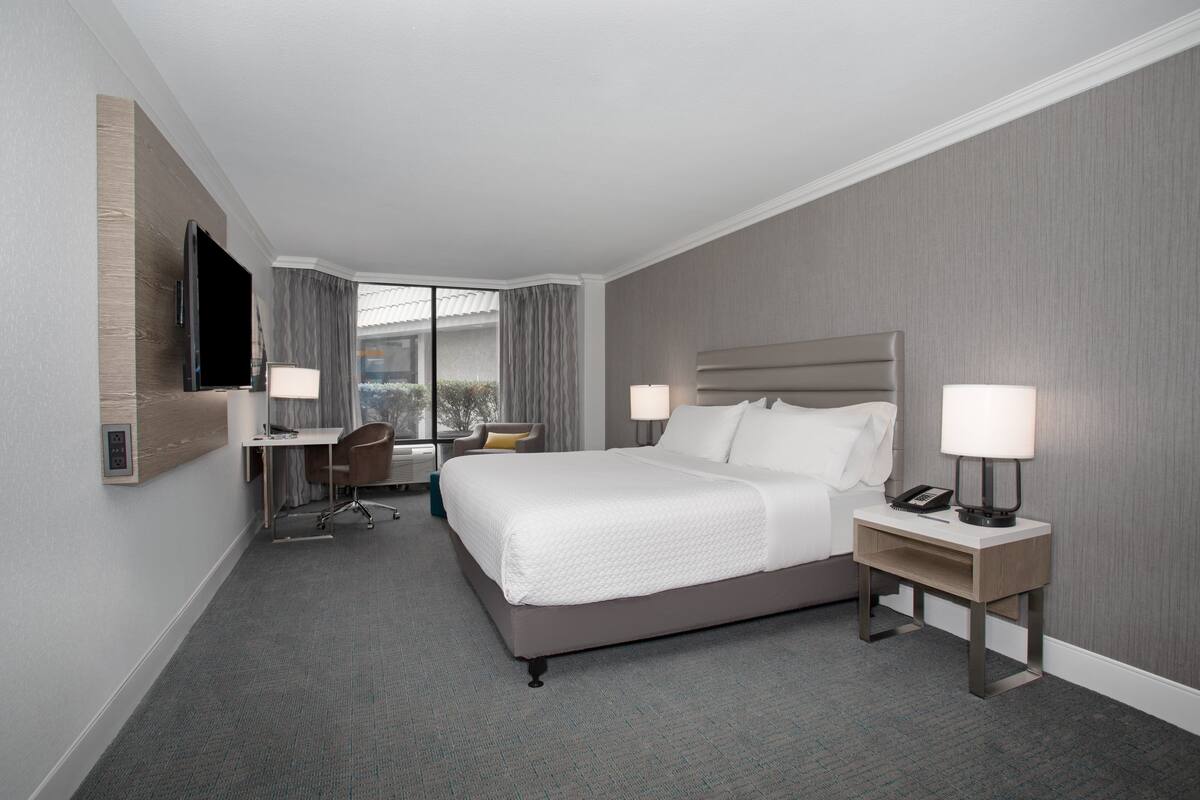 A hotel room with a large bed, a desk, a chair, and a TV mounted on the wall.