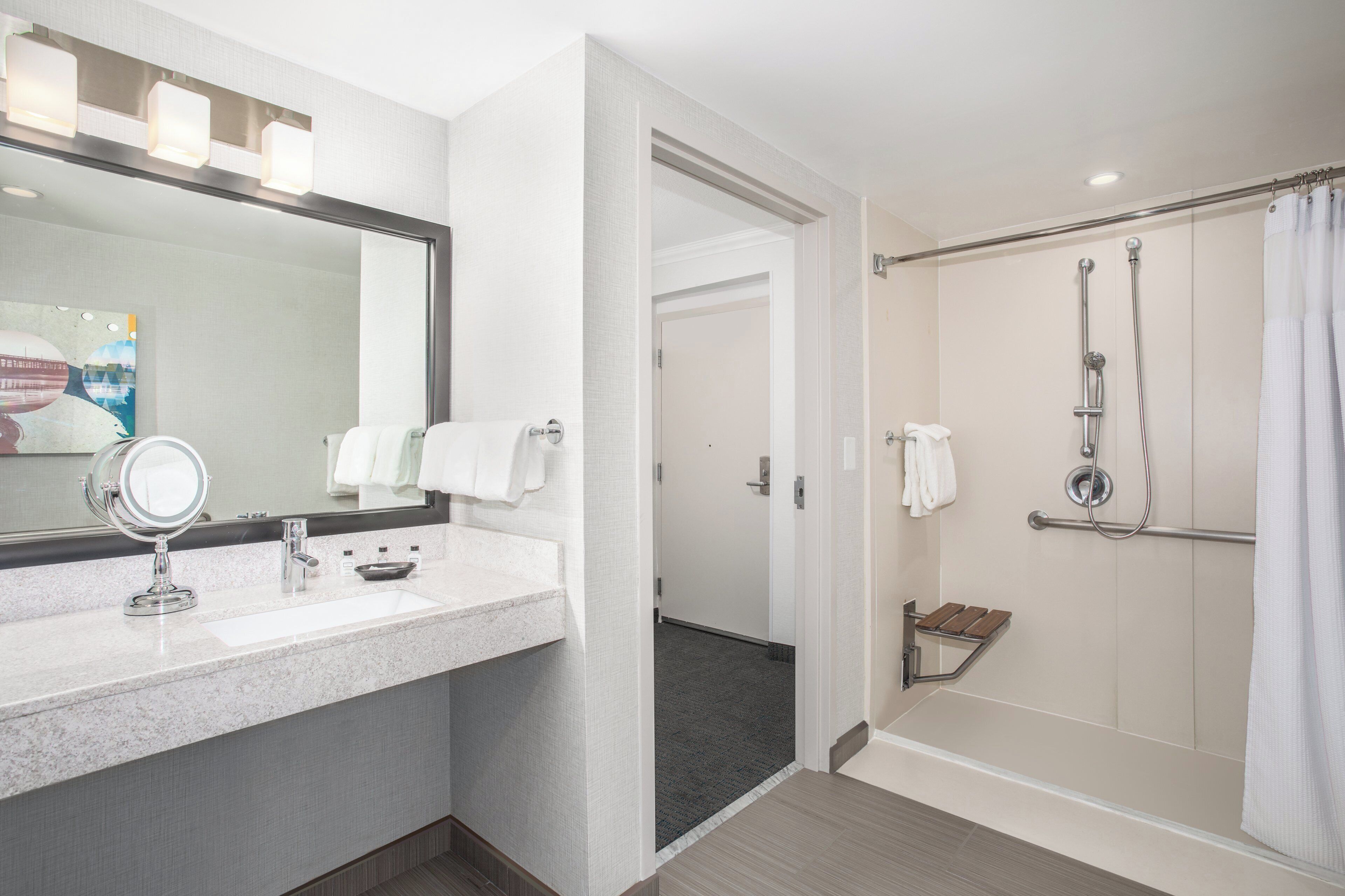 A hotel bathroom with a sink, mirror, and shower.