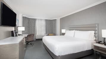 Ein Hotelzimmer mit Bett, Nachttisch, Schreibtisch, Stuhl und einem Flachbildfernseher.