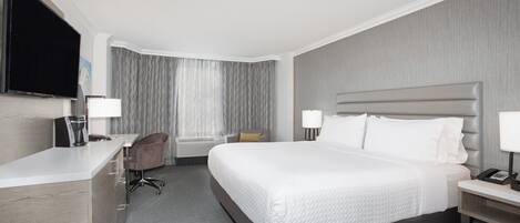 A hotel room with a bed, bedside table, desk, chair, and a flat-screen TV.
