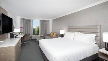 Une chambre d’hôtel avec un grand lit, un bureau avec une télévision, une chaise et une fenêtre avec des rideaux.