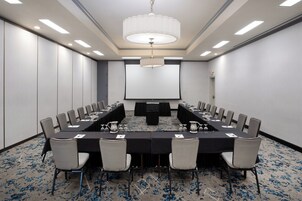Un salón de conferencias con una larga mesa, sillas, una pantalla de proyector y una araña.