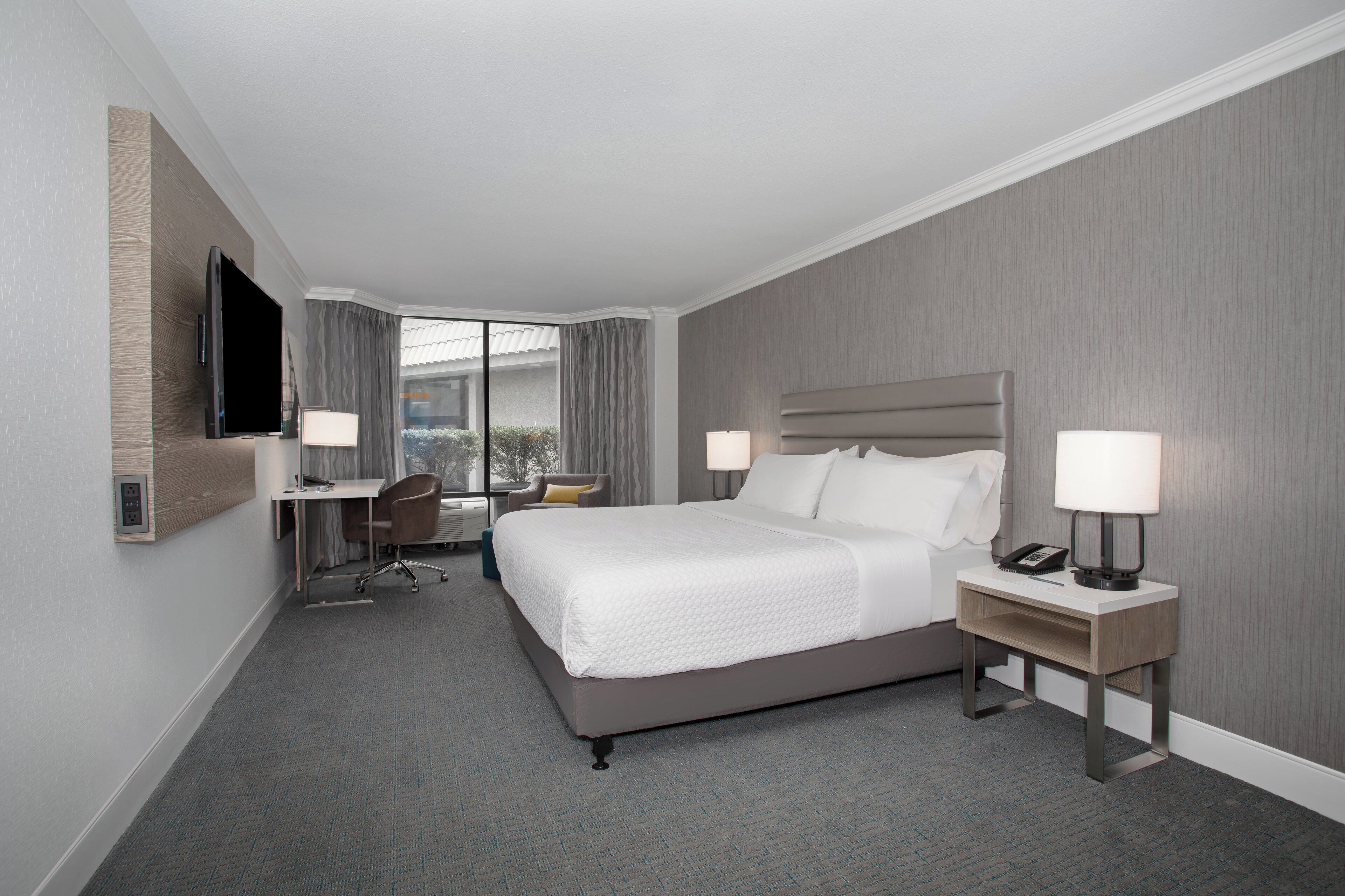 Habitación de hotel con cama, escritorio, silla y televisor montado en la pared.