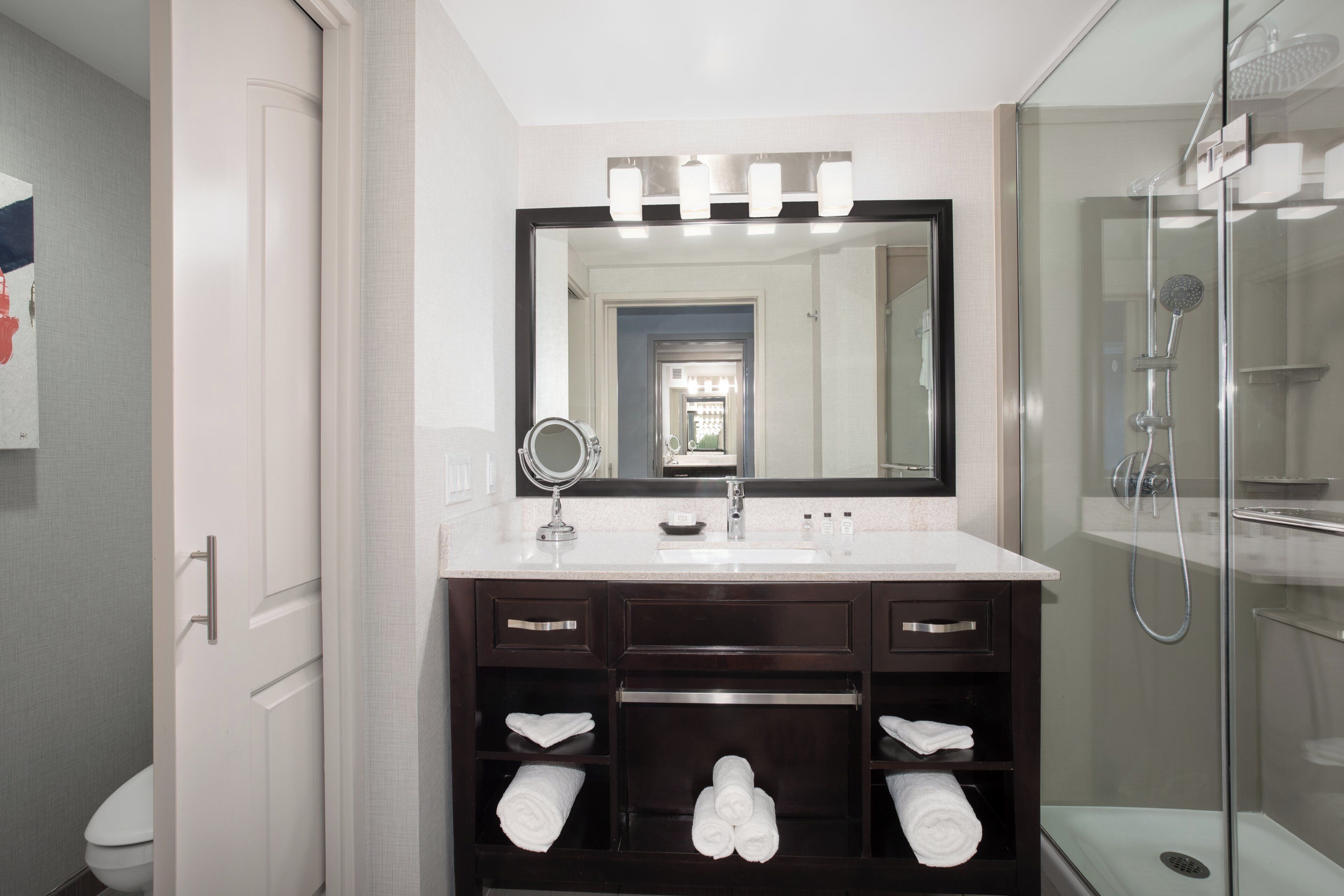 A bathroom with a white sink, dark vanity, and a glass shower enclosure.