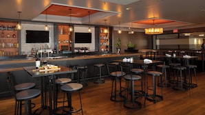 A bar area with multiple stools, a counter with a variety of bottles, and a television screen. - Crowne Plaza Costa Mesa Orange County by IHG (Costa Mesa)