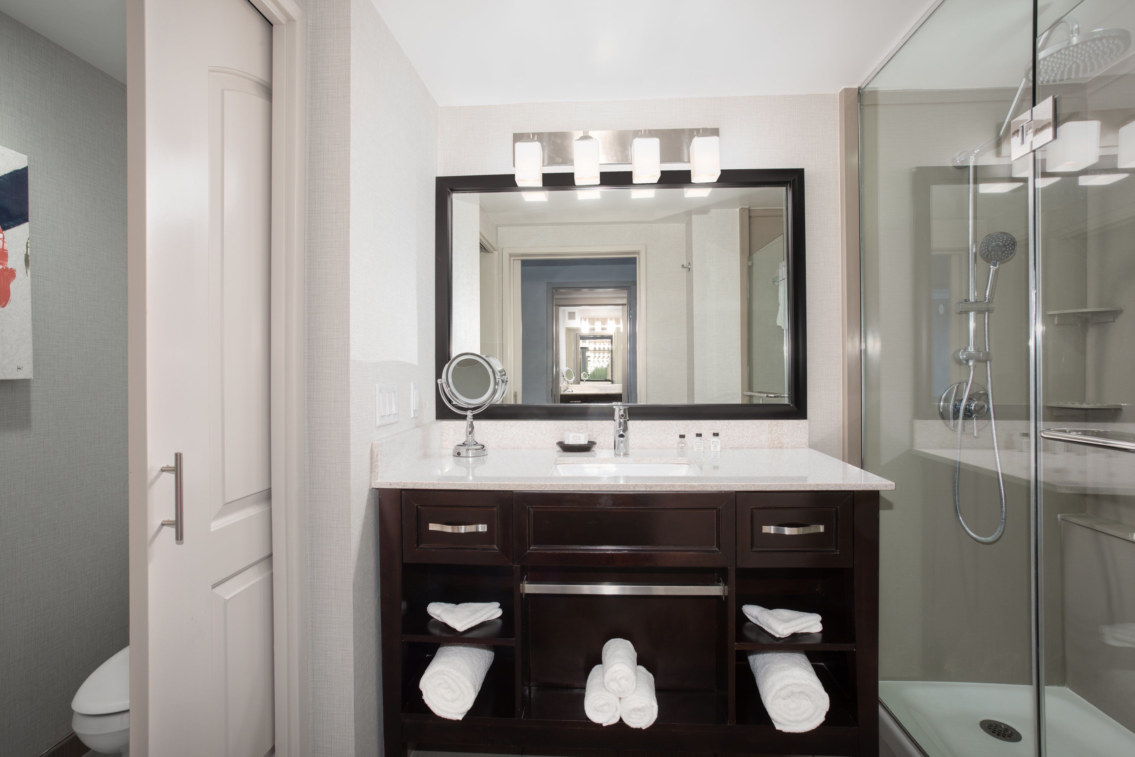 A modern bathroom with a large mirror, vanity, and a glass-enclosed shower.