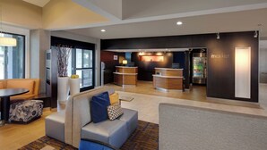 A modern hotel lobby with seating areas, a reception desk, and a minibar.