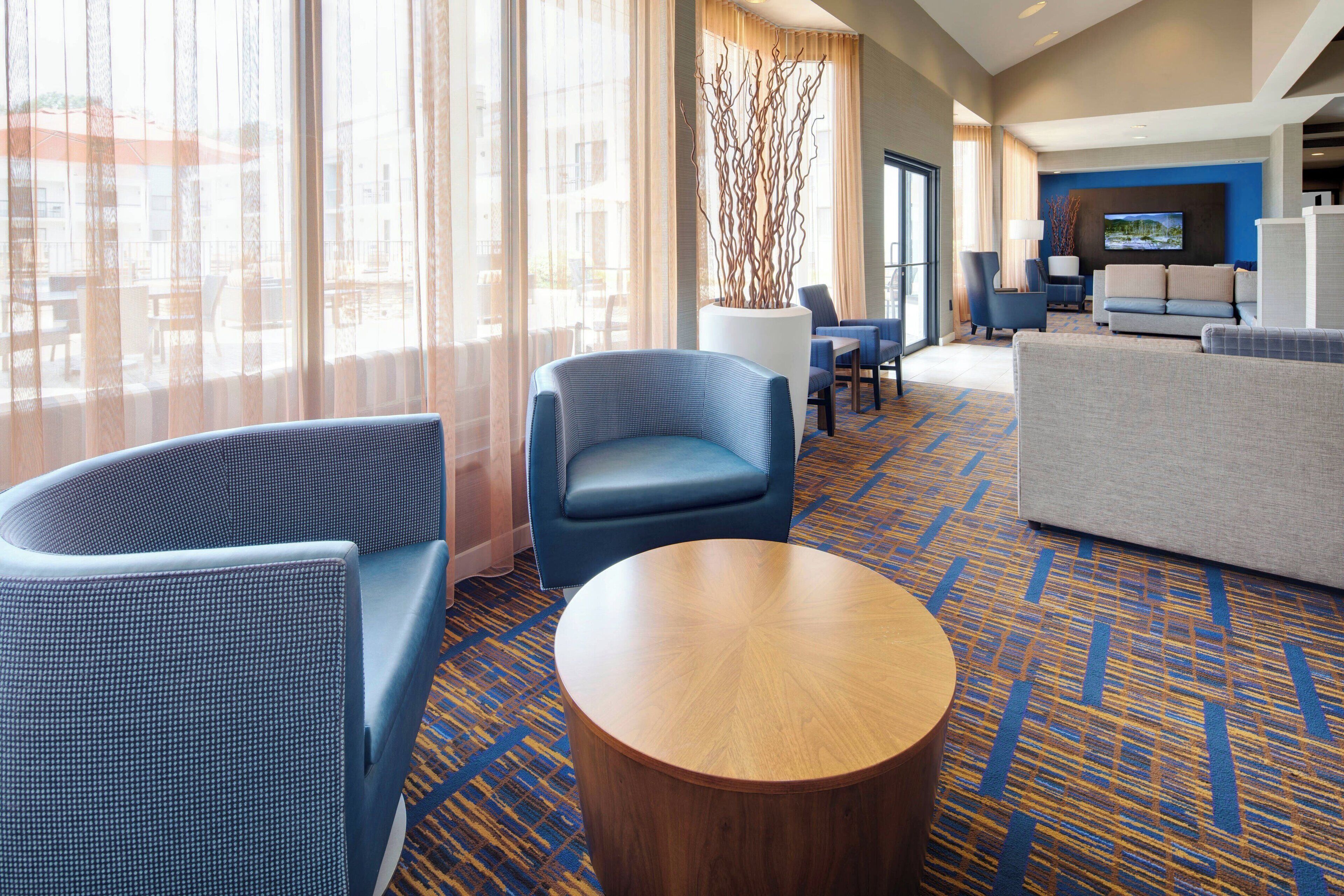 A hotel lobby with seating areas, a flat-screen TV, and a view through large windows.