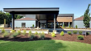 A Courtyard by Marriott hotel with a covered entrance, landscaped garden, and a clear blue sky.