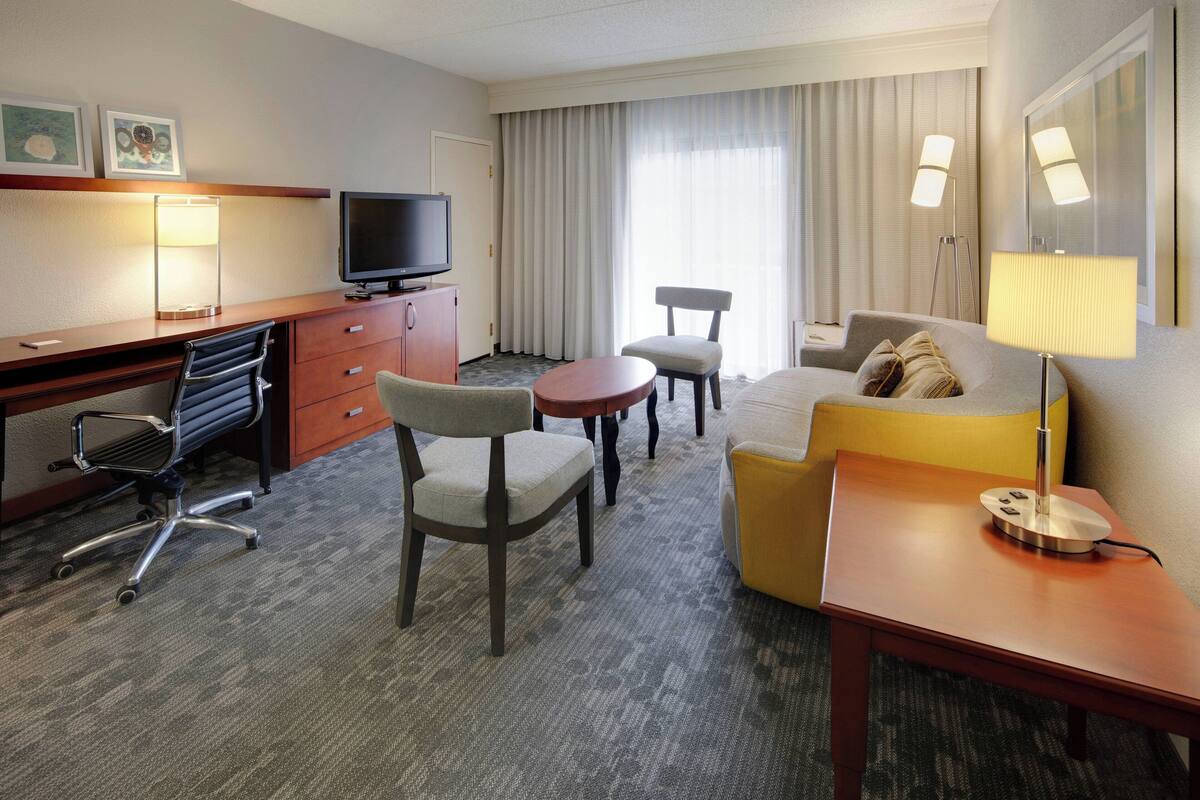 Une chambre d’hôtel équipée d’un bureau, d’une télévision, d’un canapé, d’une chaise et d’une lampe.
