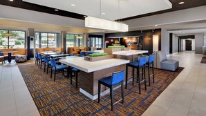 A modern hotel lobby with a central bar area, seating arrangements, and large windows providing natural light.
