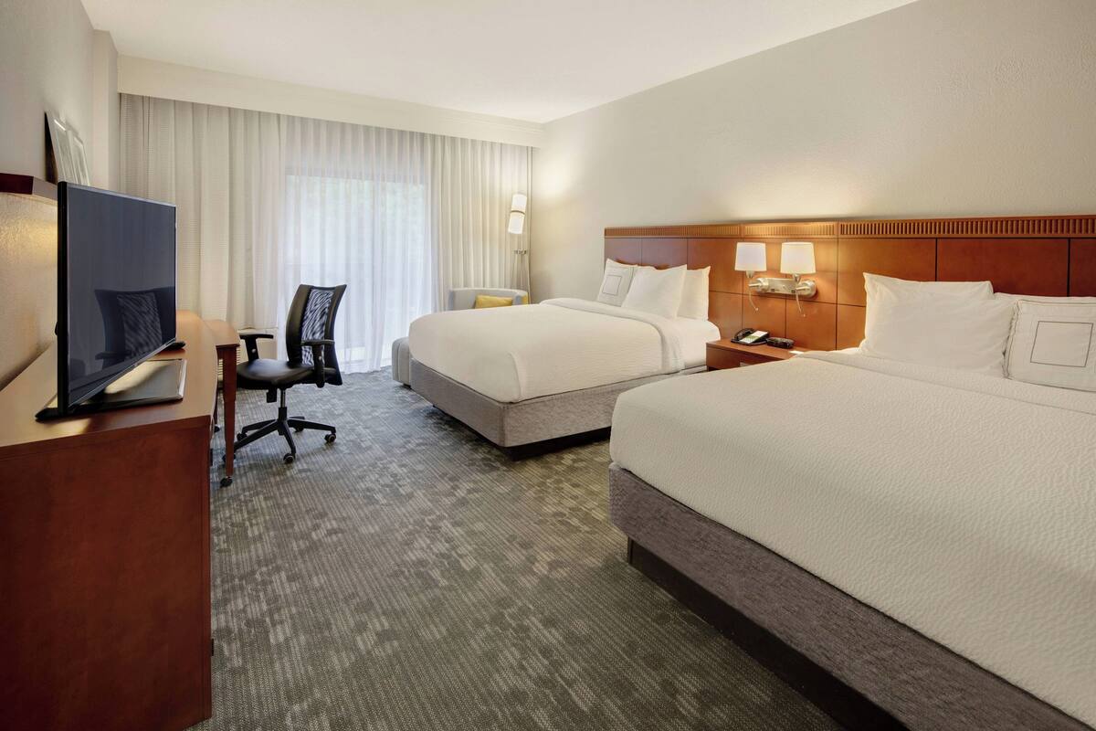 Une chambre d’hôtel avec deux lits, un bureau avec un ordinateur, une chaise et un téléviseur.