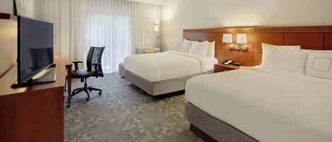 A hotel room with two beds, a desk with a computer, a chair, and a TV.
