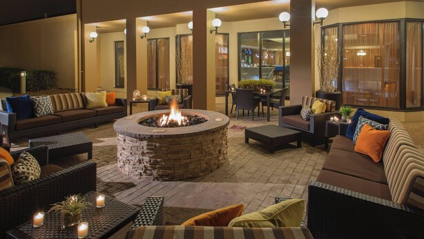 An outdoor patio area with a stone fire pit, wicker furniture, and ambient lighting.