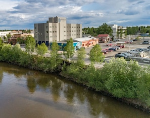 Un hôtel au design moderne, situé près d’une rivière, avec un parking et divers bâtiments en arrière-plan.