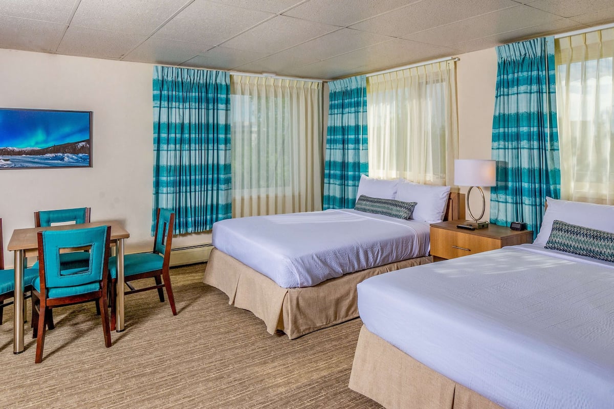 A hotel room with two beds, a desk with chairs, and a painting on the wall.
