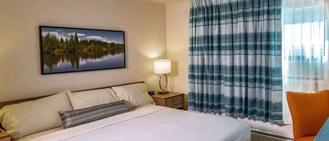 Una habitación de hotel con una cama, una mesita de noche con lámpara, una ventana con cortinas y una silla.