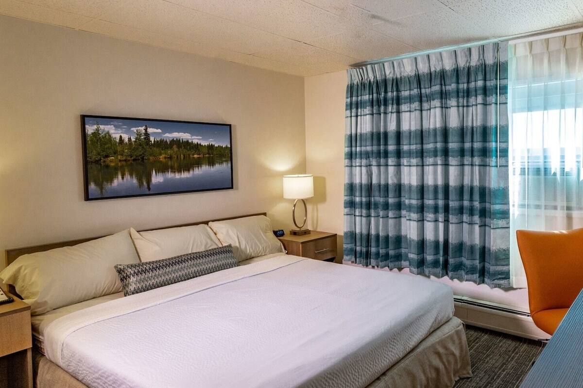A hotel room with a large bed, a desk with a chair, a coffee maker, and a view of a lake through the window.