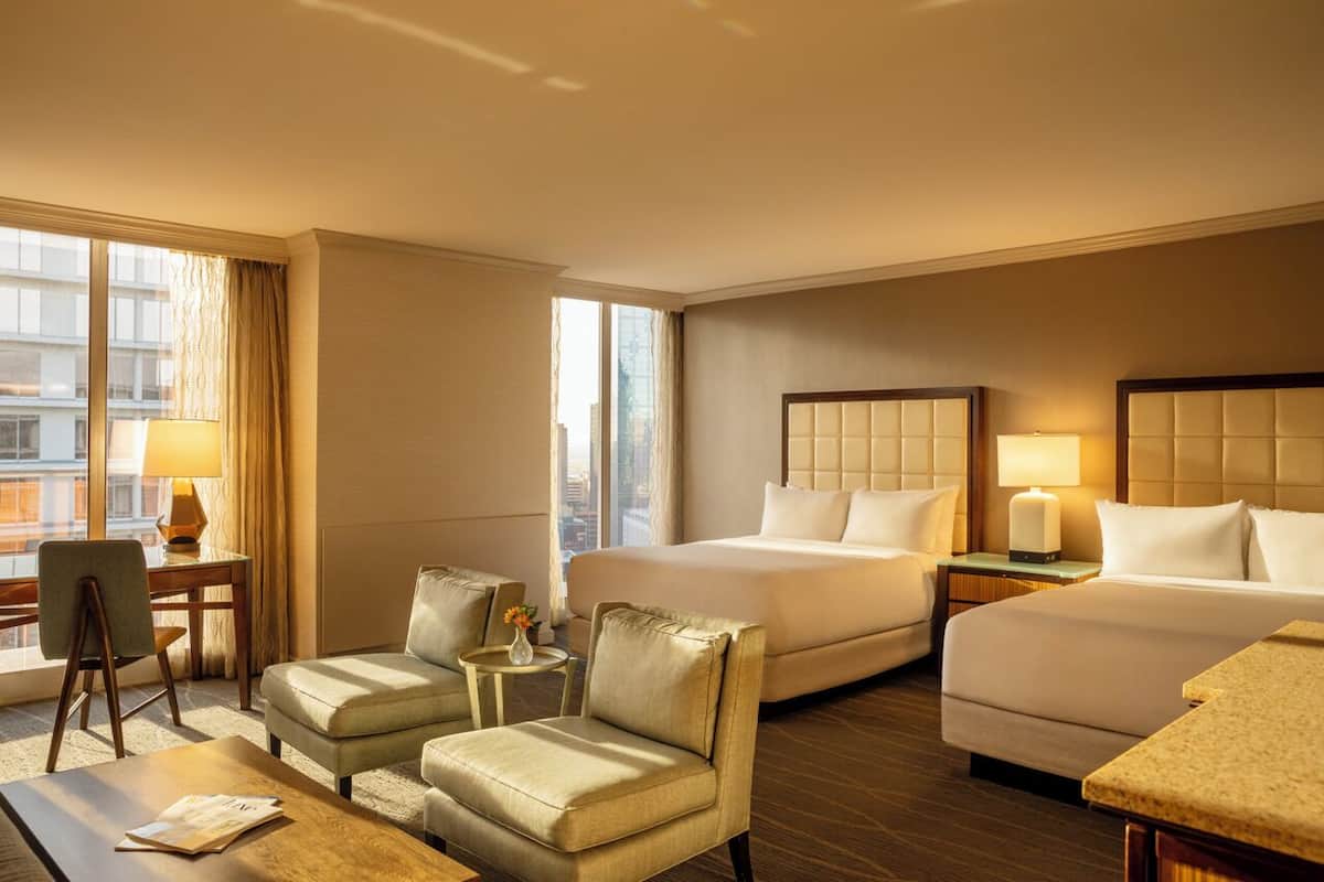 A hotel room with two beds, a desk, a chair, and a small table.