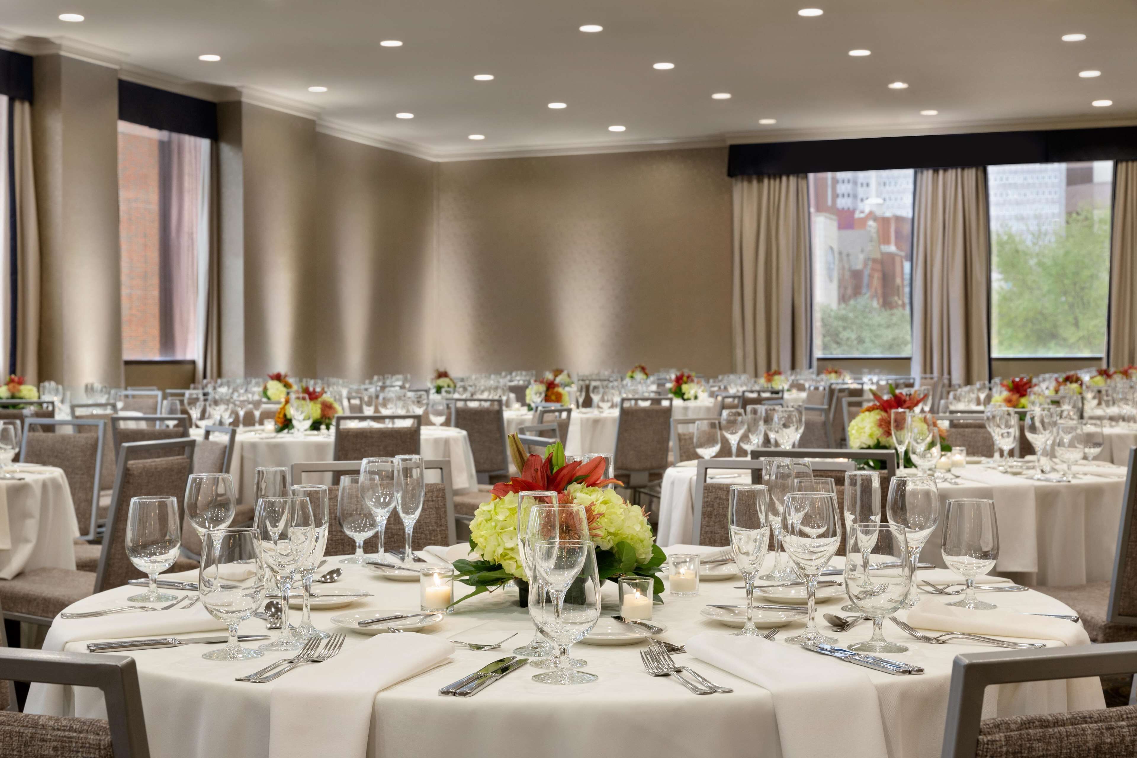 Een balzaal met ronde tafels gedekt voor een diner, met witte tafelkleden en bloemdecoraties.