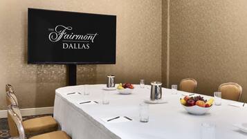 A conference room with a long table, chairs, a fruit bowl, and a coffee pot.