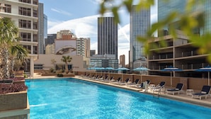 Una piscina con sillas de descanso y sombrillas, rodeada de edificios altos.