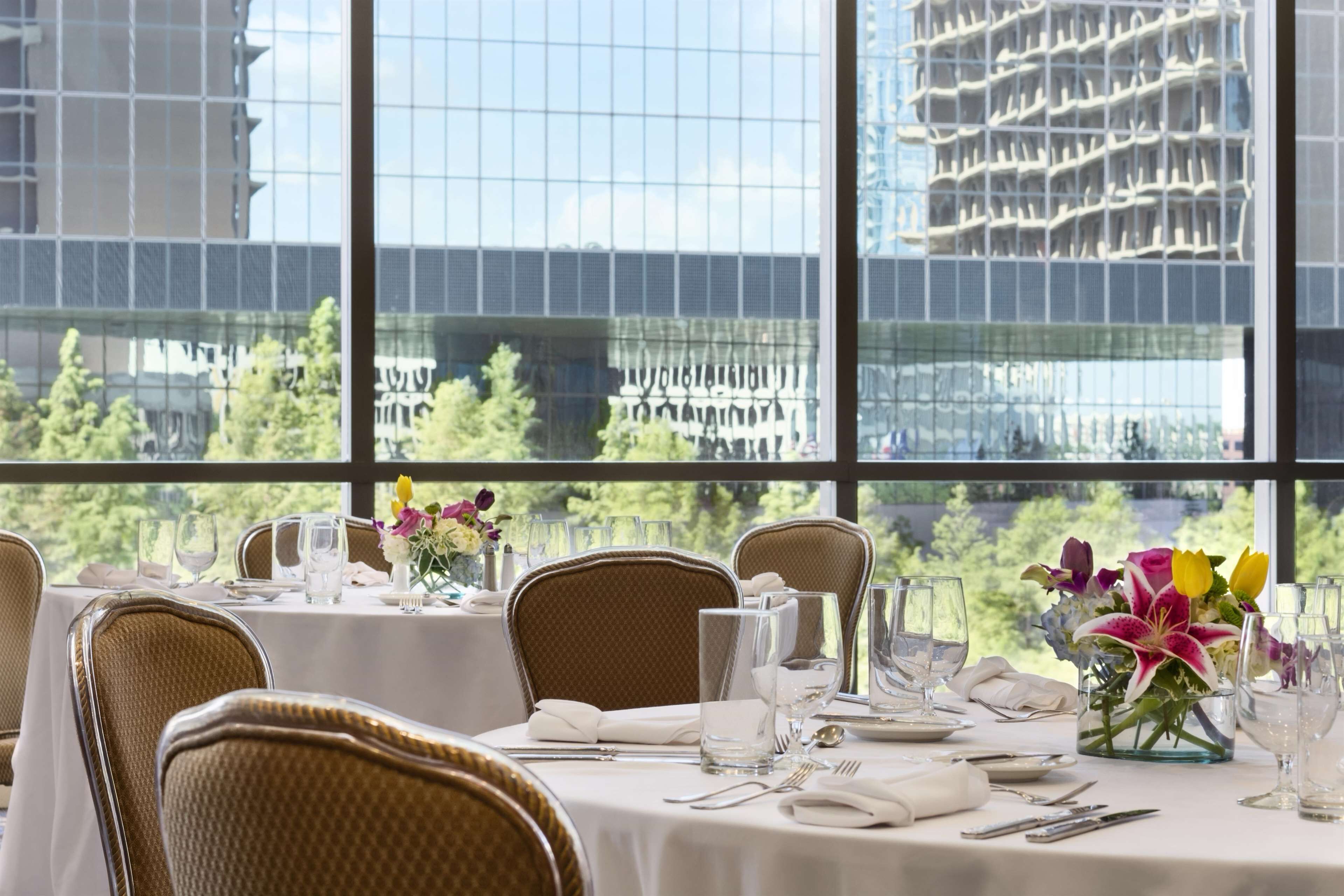 A dining area with tables set for a meal, large windows with a view of a modern building and greenery.