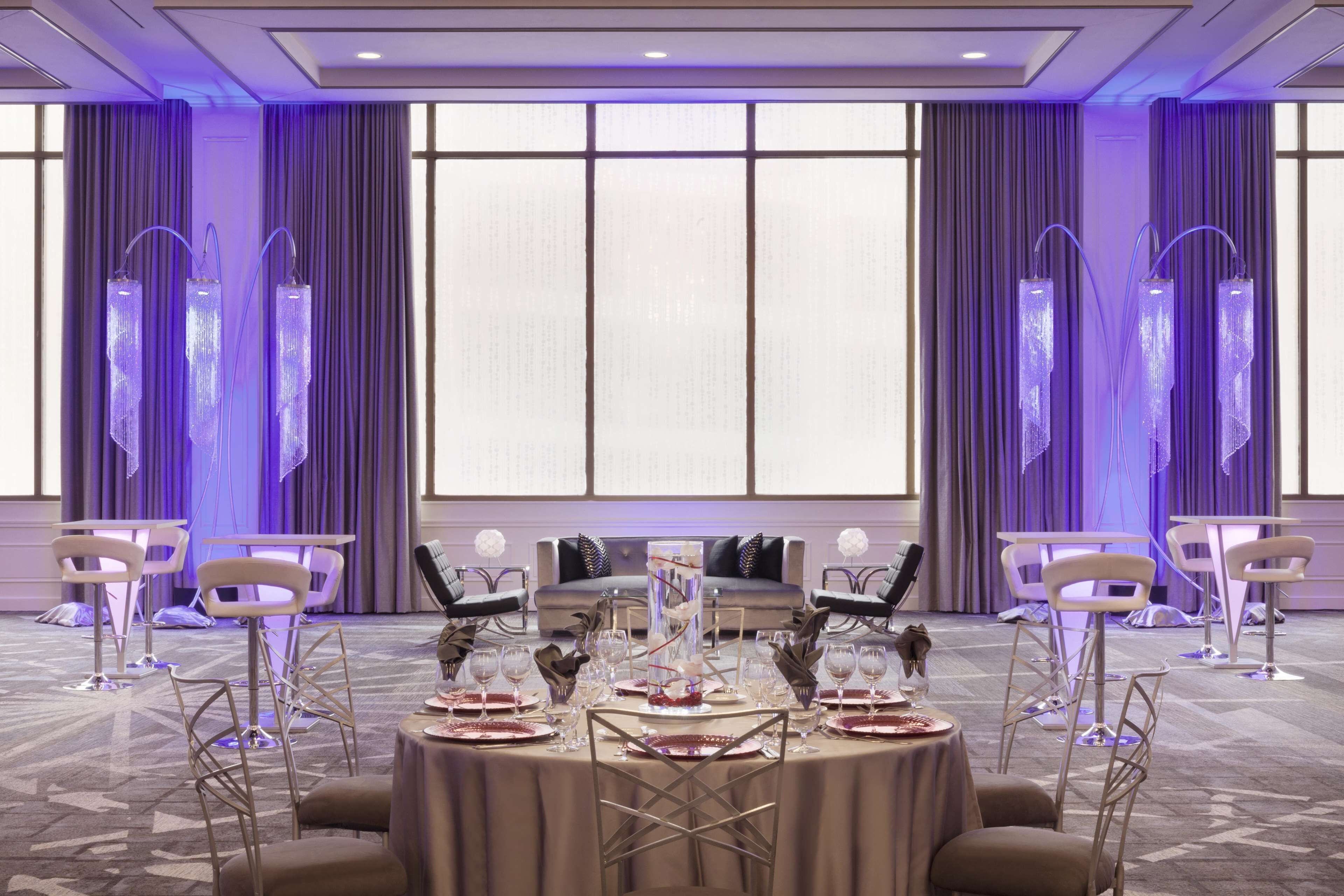 A banquet hall with round tables set for dining, a sofa, and tall, illuminated columns.