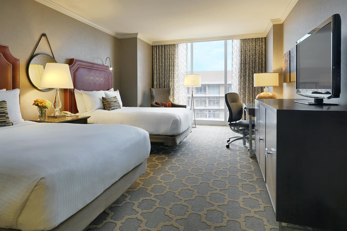 A hotel room with two beds, a desk with a TV, and a view of the city.