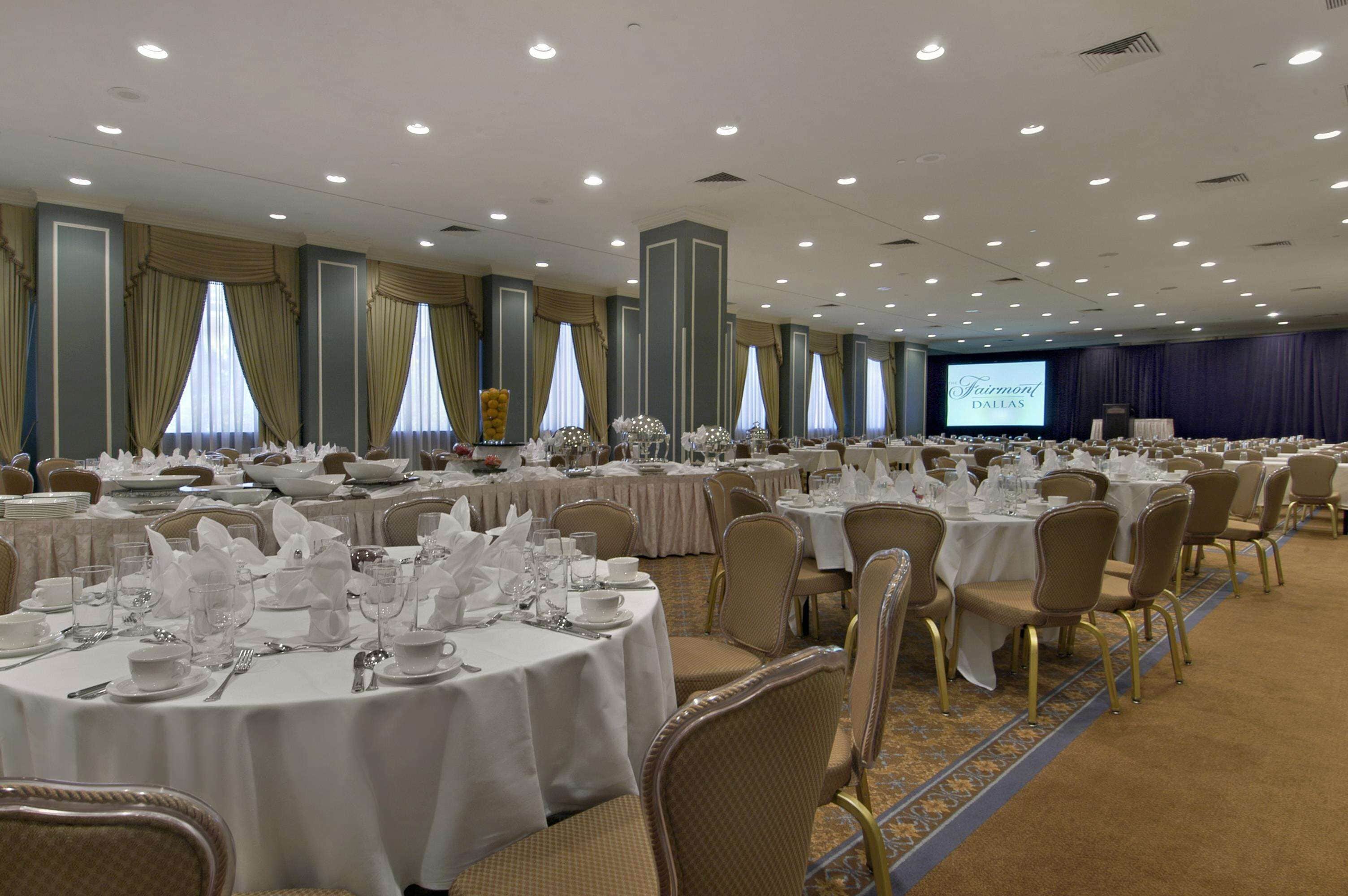 Un salón de banquetes con mesas redondas dispuestas para cenar, un escenario con una pantalla y suelo alfombrado.