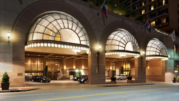 Fachada de hotel con un gran arco, varias banderas y un interior bien iluminado.