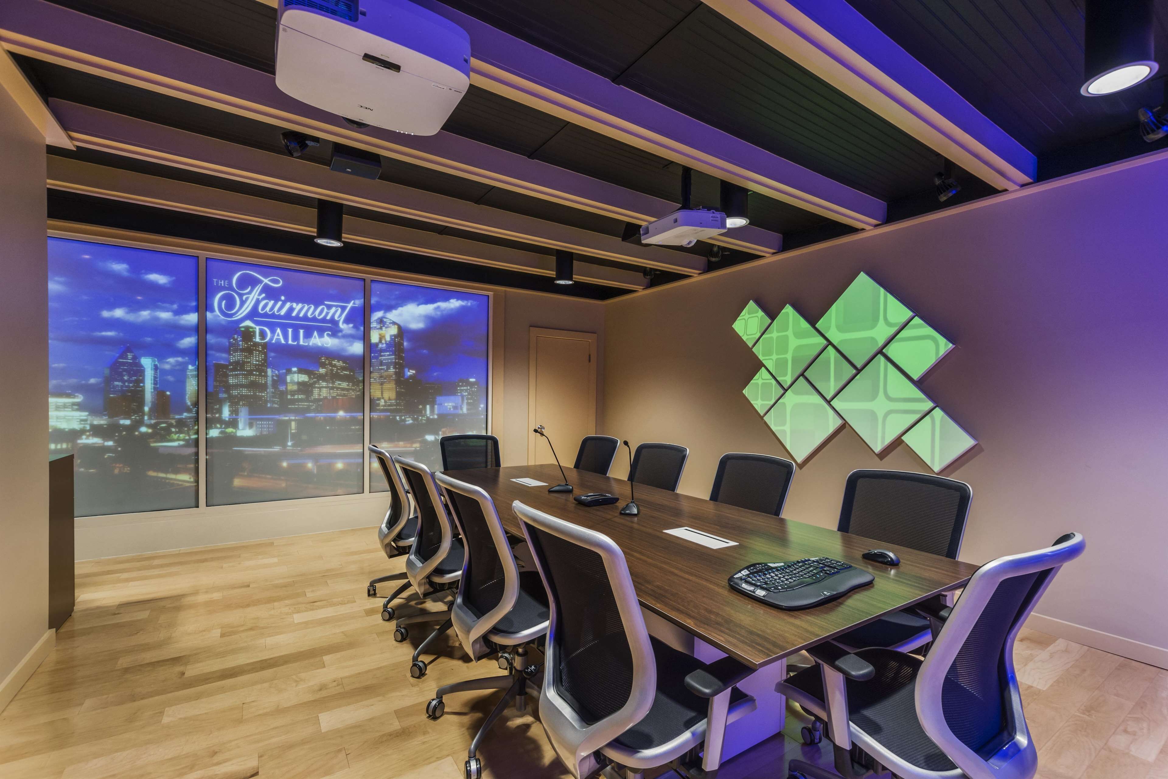 Un salón de conferencias con una gran mesa, sillas, un proyector y una pantalla que muestra un paisaje urbano.