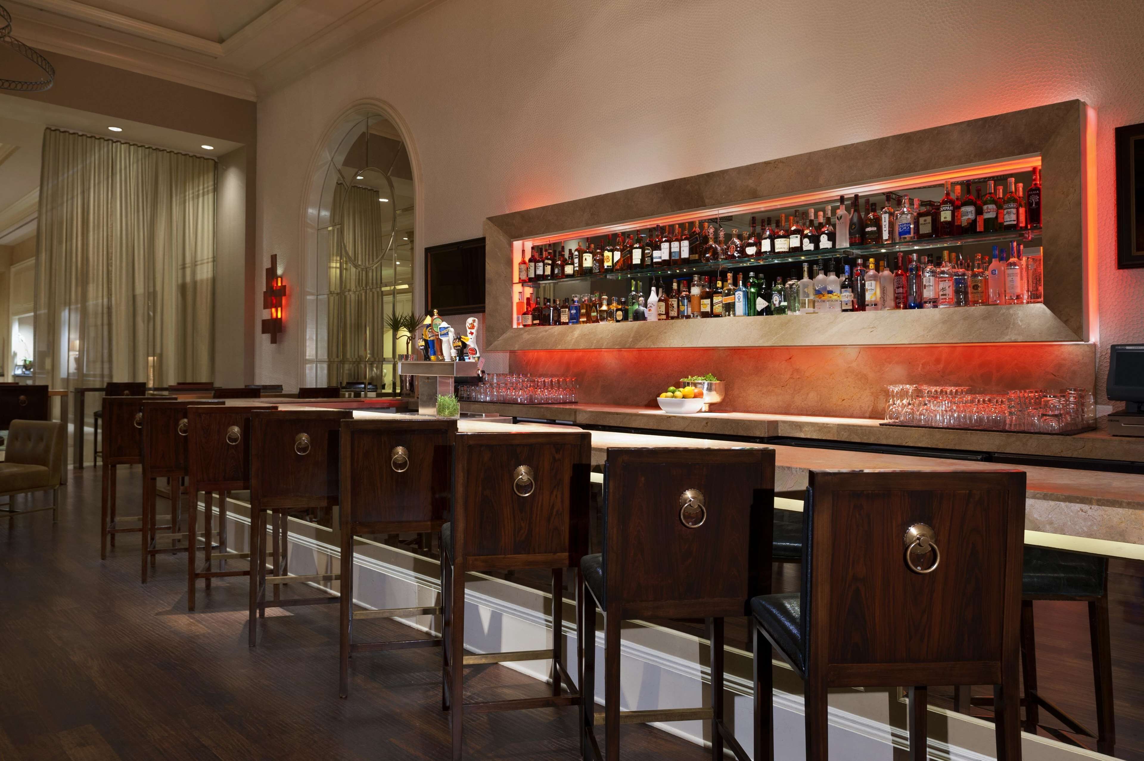 Een bar met houten stoelen, een toog en kasten vol flessen.