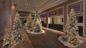 Un vestíbulo con tres grandes árboles de Navidad iluminados, una imponente escalera y una chimenea.