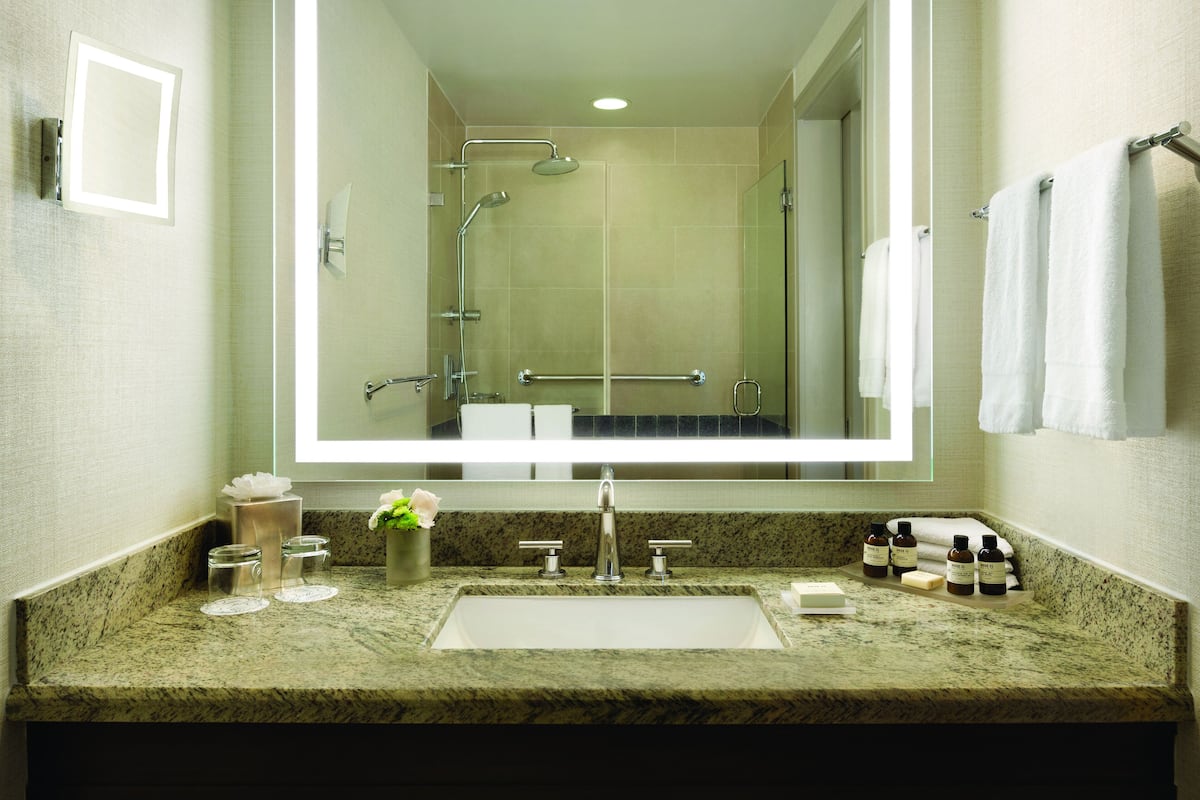 A bathroom with a large mirror, a sink with a marble countertop, and a shower area.