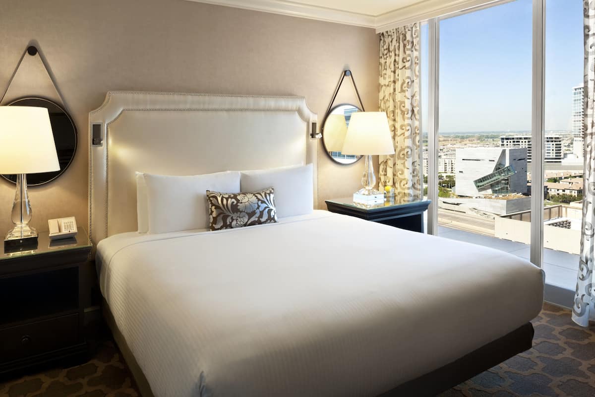 A hotel room with a large bed, two bedside tables with lamps, a view of the city through large windows.