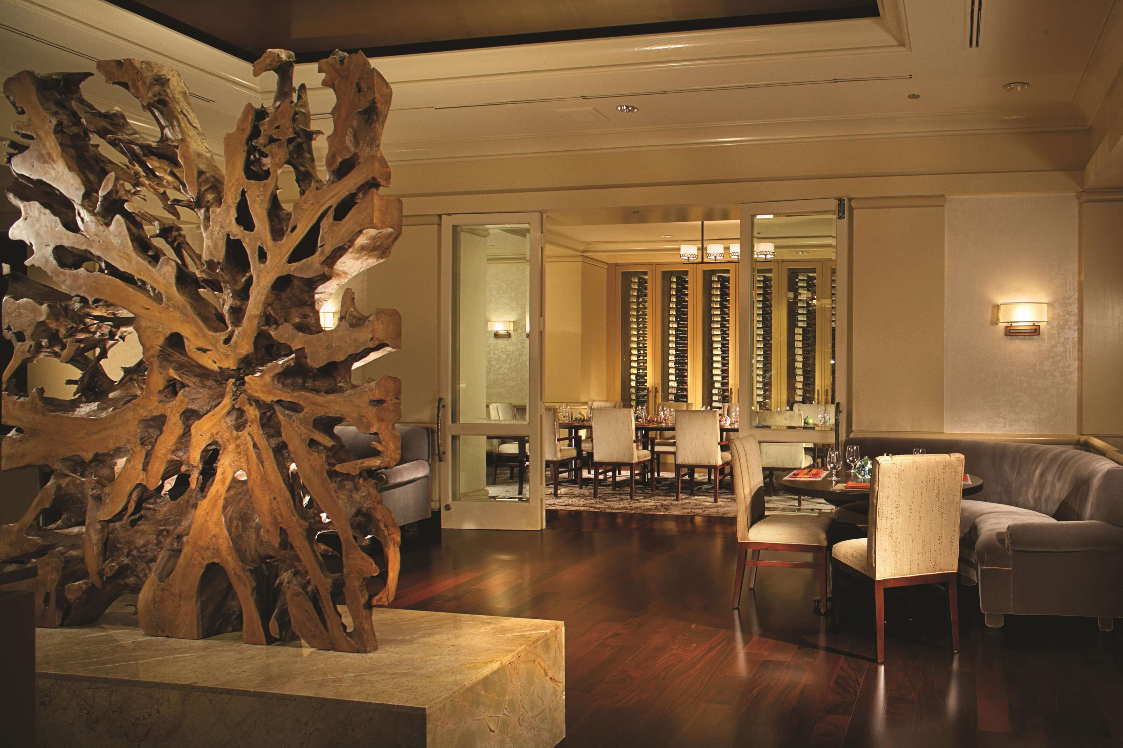A spacious living room with a large wooden sculpture, a modern sofa, and a dining area with a chandelier.
