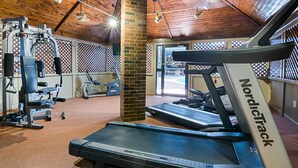 Une salle de sport équipée de tapis de course, d’appareils de musculation et d’un pilier en briques.