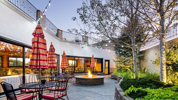 Une terrasse extérieure avec des tables et des chaises rondes, un foyer et des parasols à rayures.