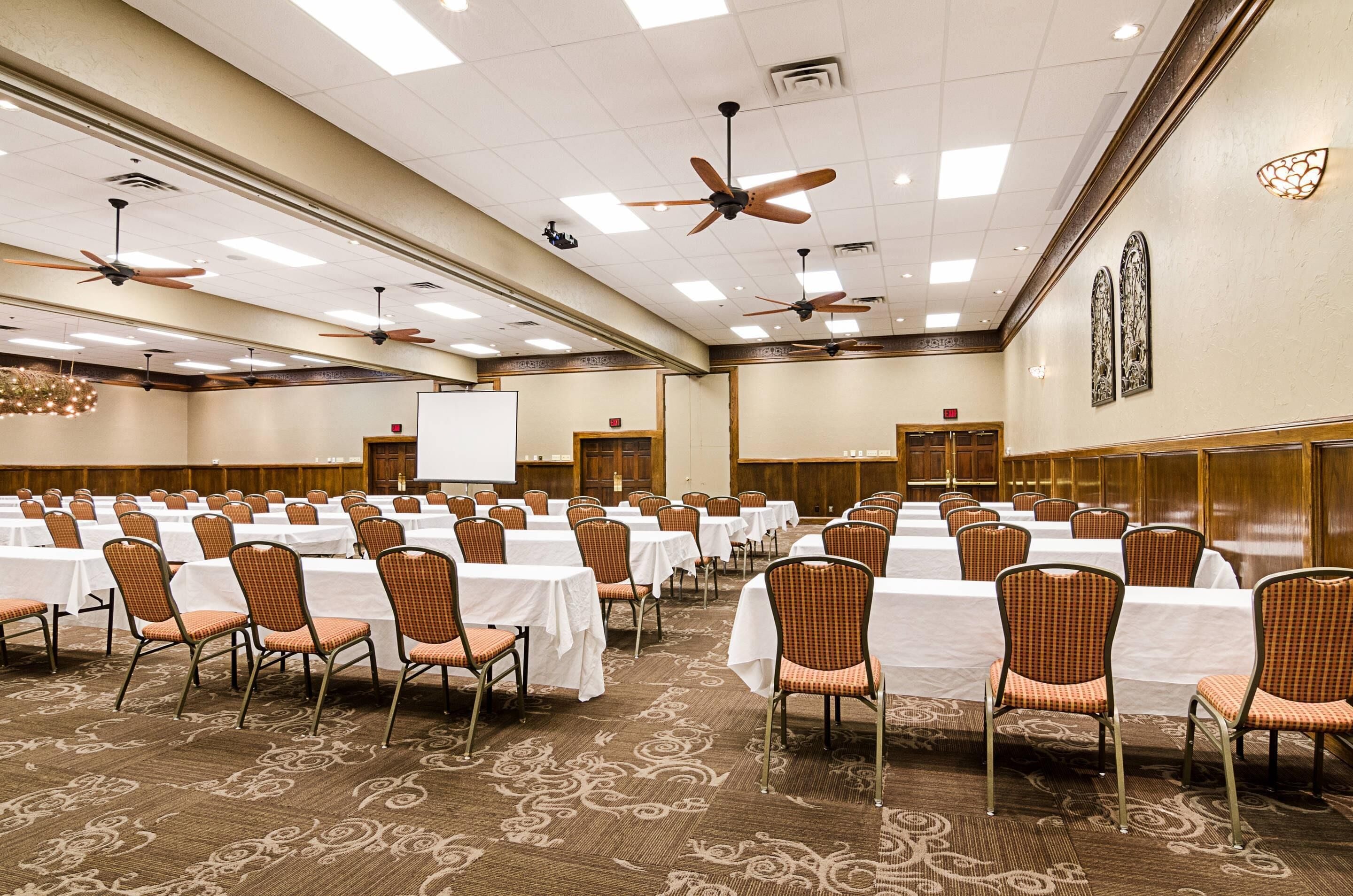 A large conference room with rows of tables and chairs, ceiling fans, and a carpeted floor.