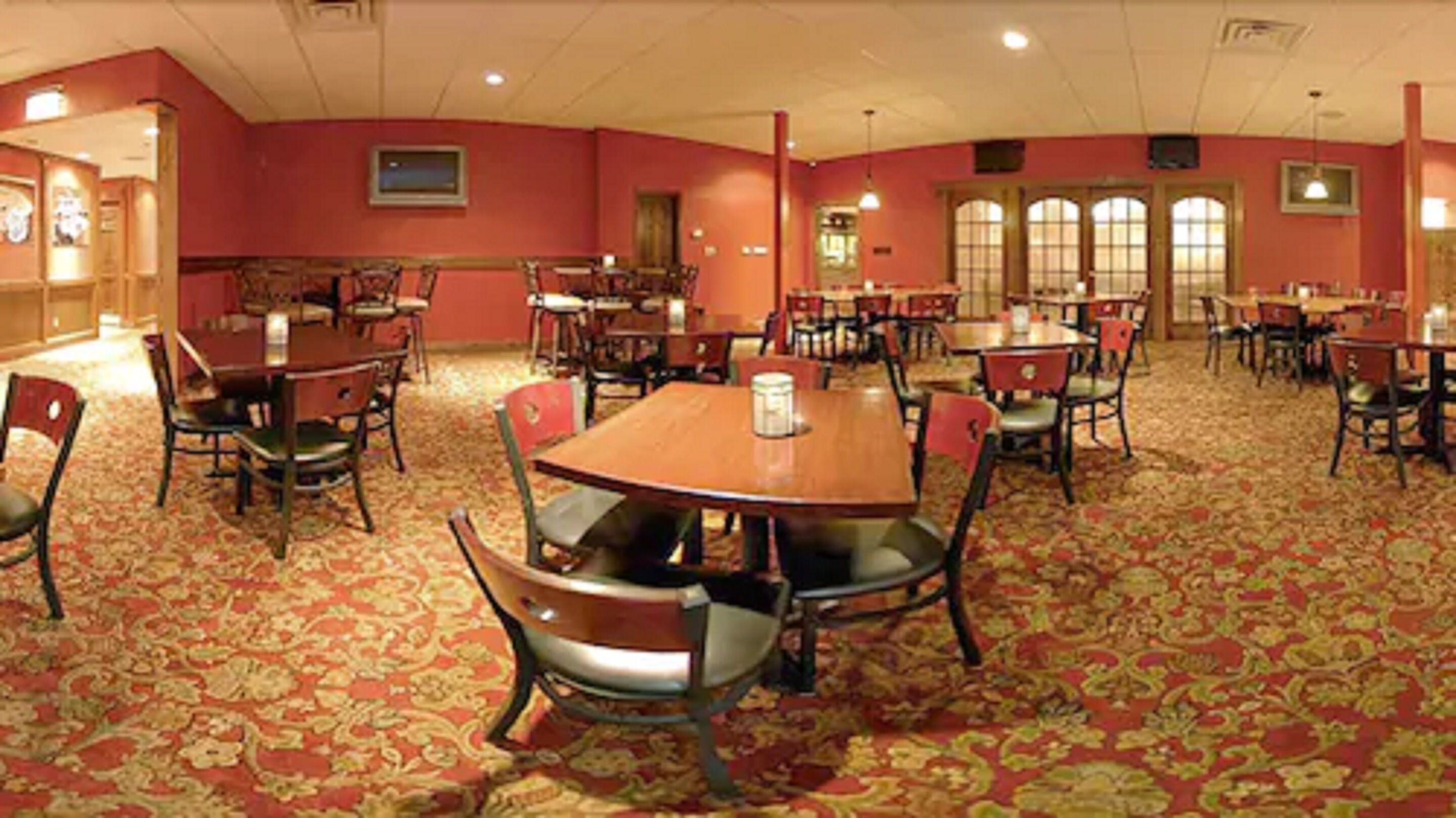 Een restaurant in een hotel met meerdere tafels en stoelen, vloerbedekking en grote ramen.