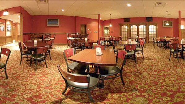 A hotel dining area with multiple tables and chairs, carpeted flooring, and large windows.