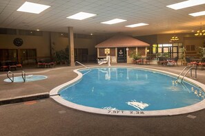 An indoor swimming pool with a lifeguard station, lounge area, and a small building with a red roof. - Clarion Inn Garden City (Garden City)