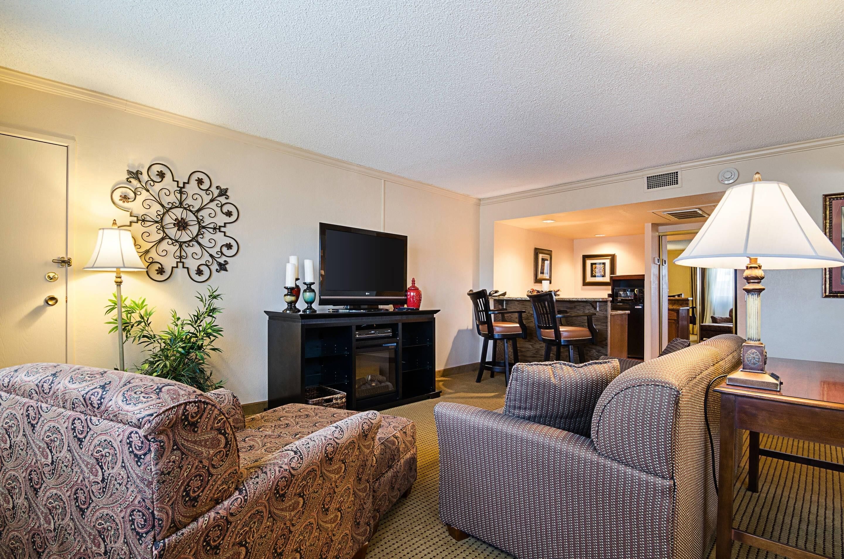 A hotel room with a sofa, a television, a dining area, and a lamp.