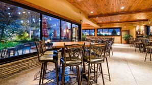 Un restaurant doté d’un plafond en bois, de grandes fenêtres et offrant une vue sur les arbres et les lumières de la ville.