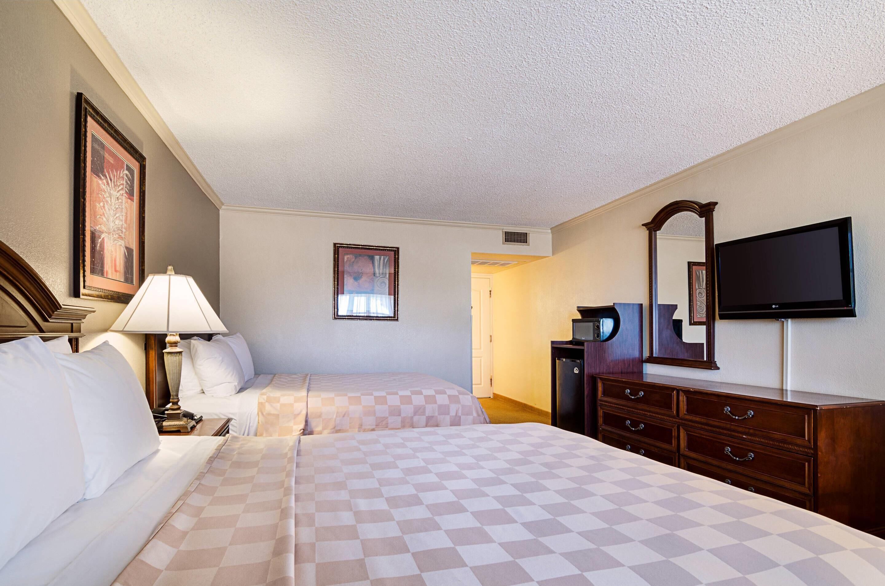 Une chambre d’hôtel avec deux lits, une télévision, une commode et un tableau encadré au mur.